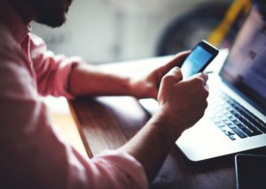 Photo of a person using a phone in front of a computer