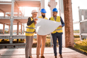 Photo of construction workers in hard hats looking at architecture blueprint