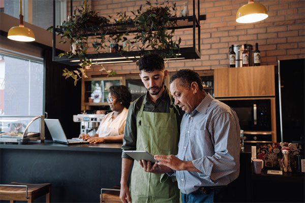 Image of ta businessowner and his employee looking at a tablet in a café